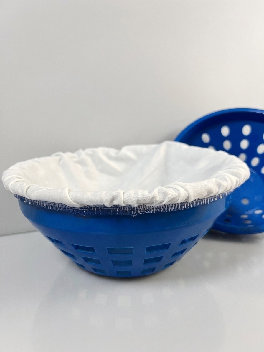 Blaues Kunststoff-Gärkörbchen (Rundform) mit Leineneinsatz, dahinter ein gelochtes Simperl